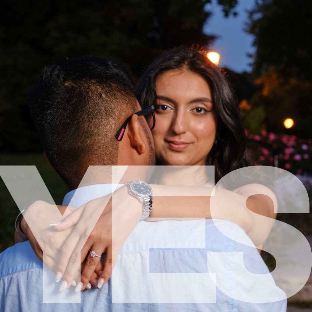 A couple with a female facing the camera with her ring highlighted. A transparent overlay says yes. Her ring is positioned between the Y and the E in yes.