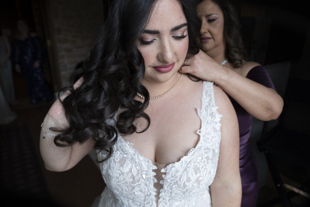 The mother of the bride helps her daughter, the bride, put on her necklace in her bridal suite at the Elora Mill, in Elora Ontario.