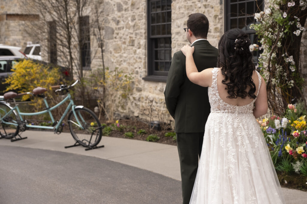 The bride touches the shoulder of her groom for the first look outside of the Elora Mill, in Elora Ontario.