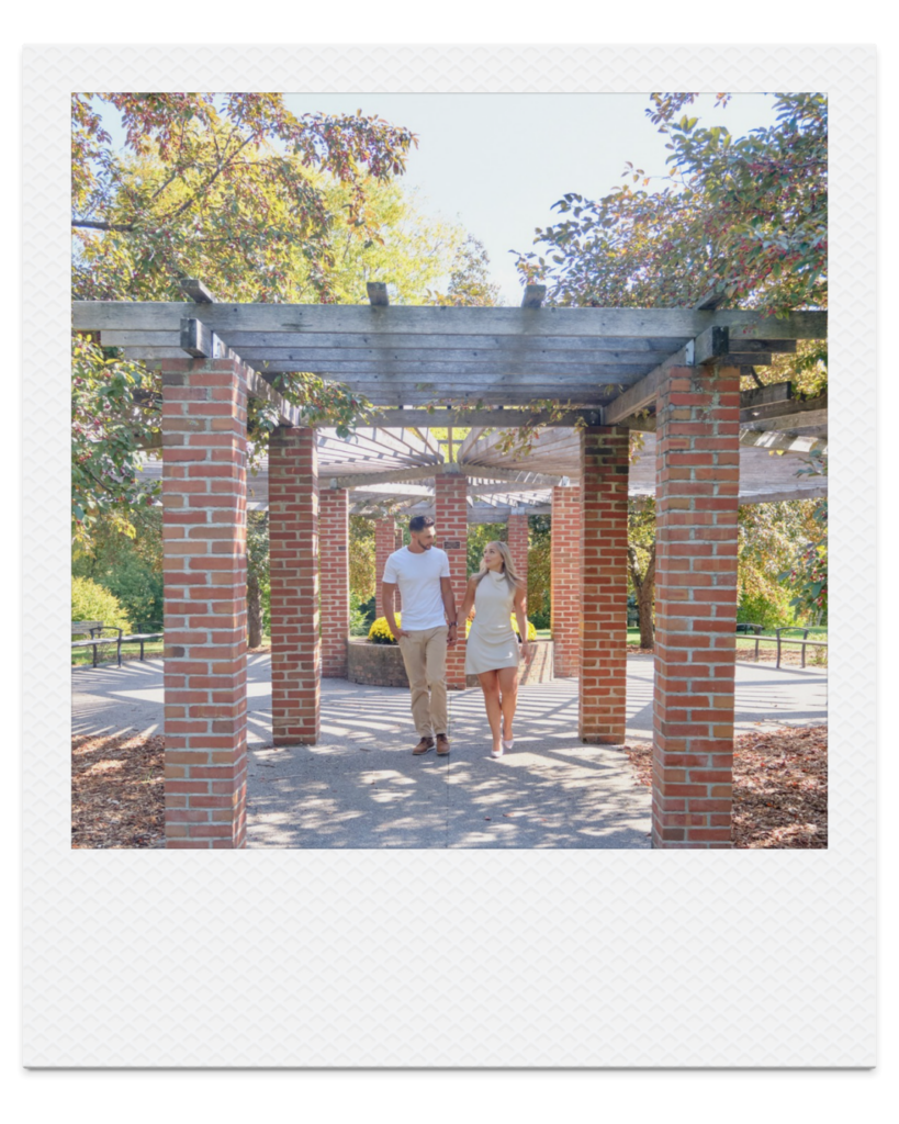 Couple walking beneath the pergola during a fall engagement session at the Collingwood Arboretum.