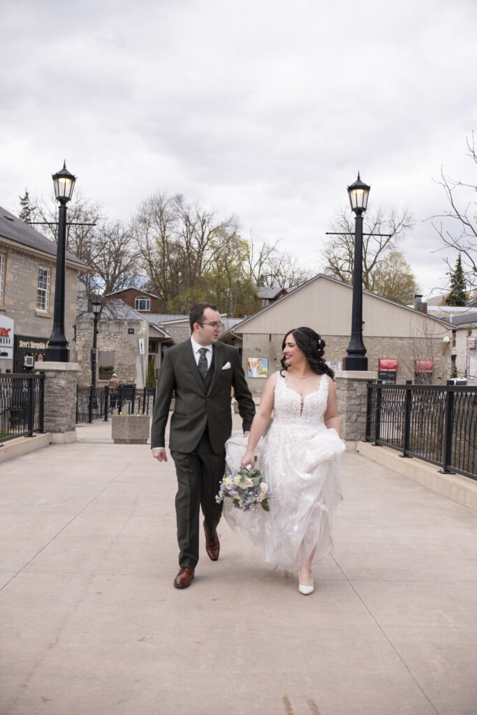 A wedding couple walking over the bridge to the chapel during an Elora Mill wedding in Elora, Ontario.