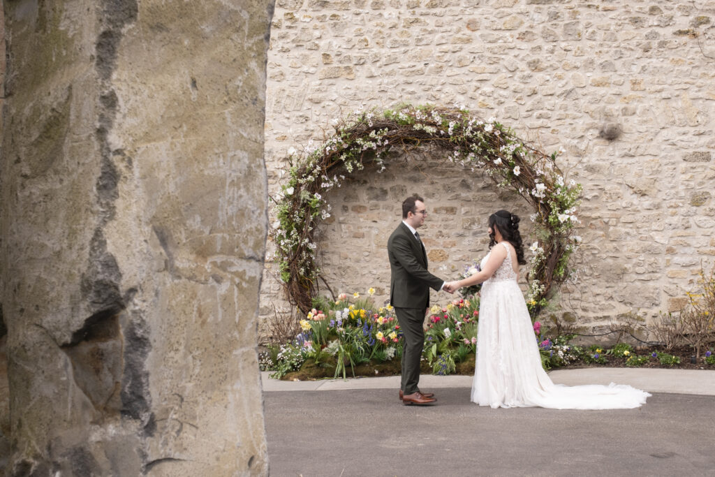 A wedding couple sharing their first look beneath a floral arch during an Elora Mill wedding in Elora, Ontario.