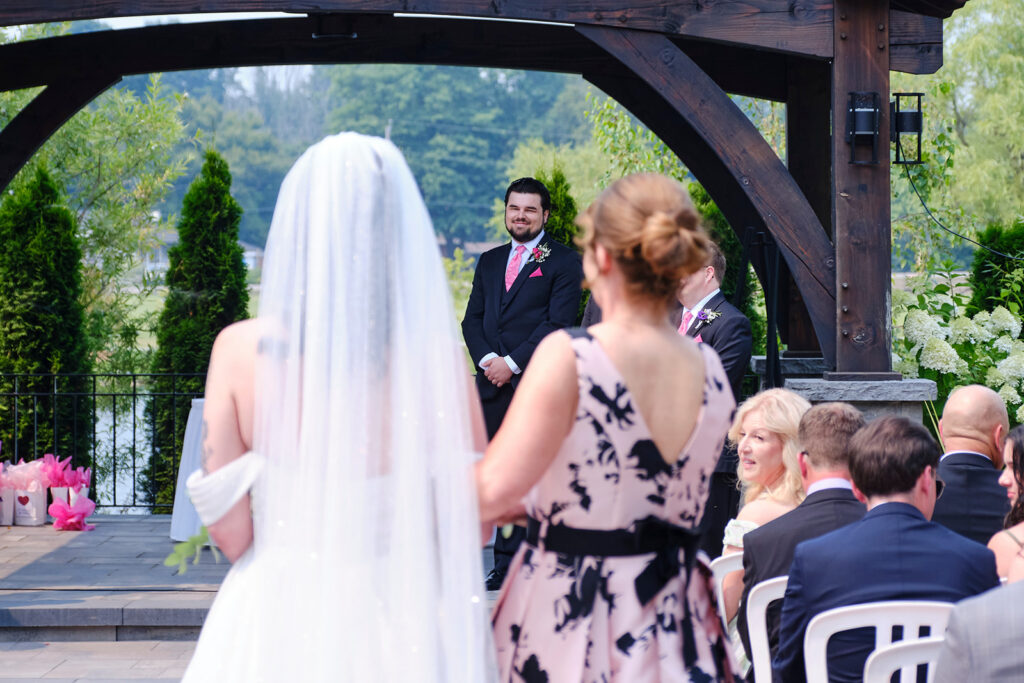 A groom watching his bride walk up the aisle in their summer wedding at Nottawasaga Inn Resort & Conference Centre during their wedding day in Alliston, Ontario.