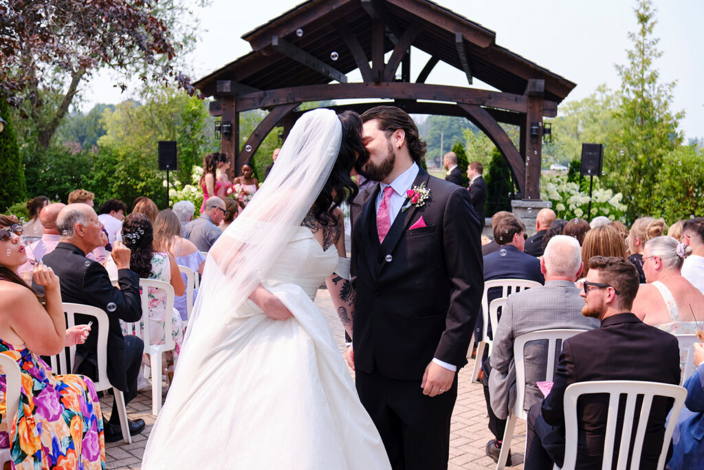 Couple share a kiss at the end of the aisle in an outdoor ceremony at Nottawasaga Inn Resort & Conference Centre during their wedding day in Alliston, Ontario.